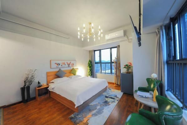 Un dormitorio moderno con una cama grande, una araña, una mesita con una silla y vistas al exterior a través de una ventana.