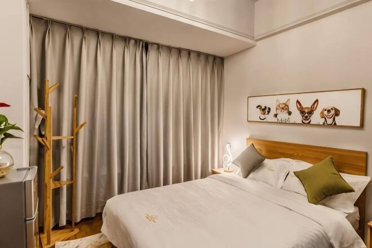 Un dormitorio con cama, mesita de noche, lámpara, perchero y ventana con cortinas.