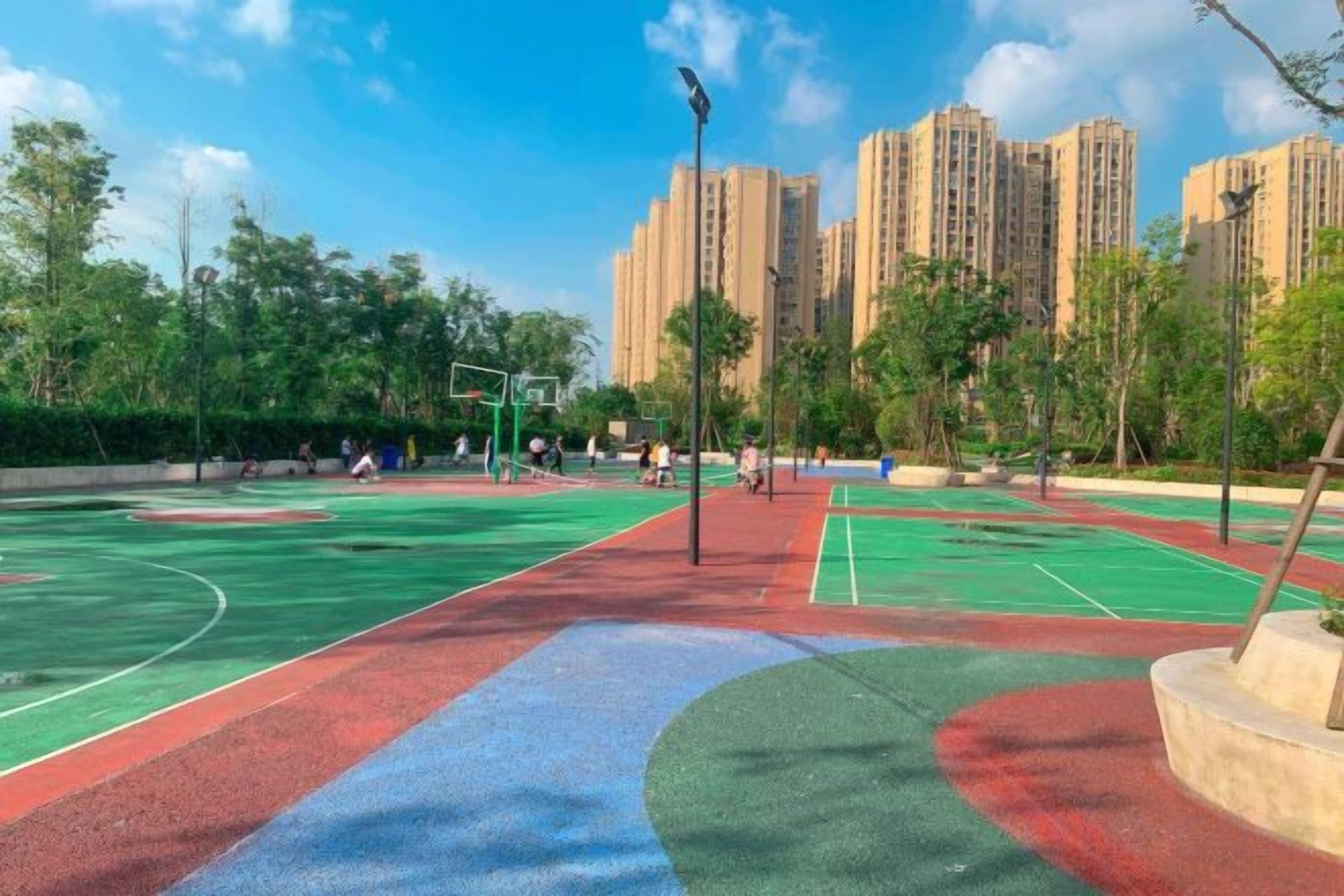 An outdoor basketball court with multiple courts, surrounded by trees and buildings in the background.