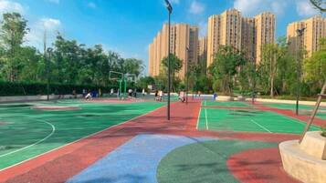 An outdoor basketball court with multiple courts, surrounded by trees and buildings in the background.