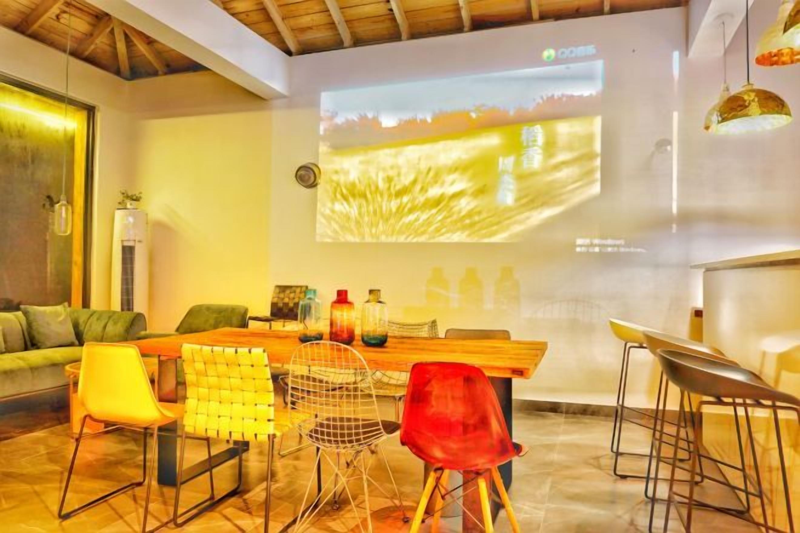 A modern living room with a wooden dining table, bar stools, and a large screen displaying a landscape projection.