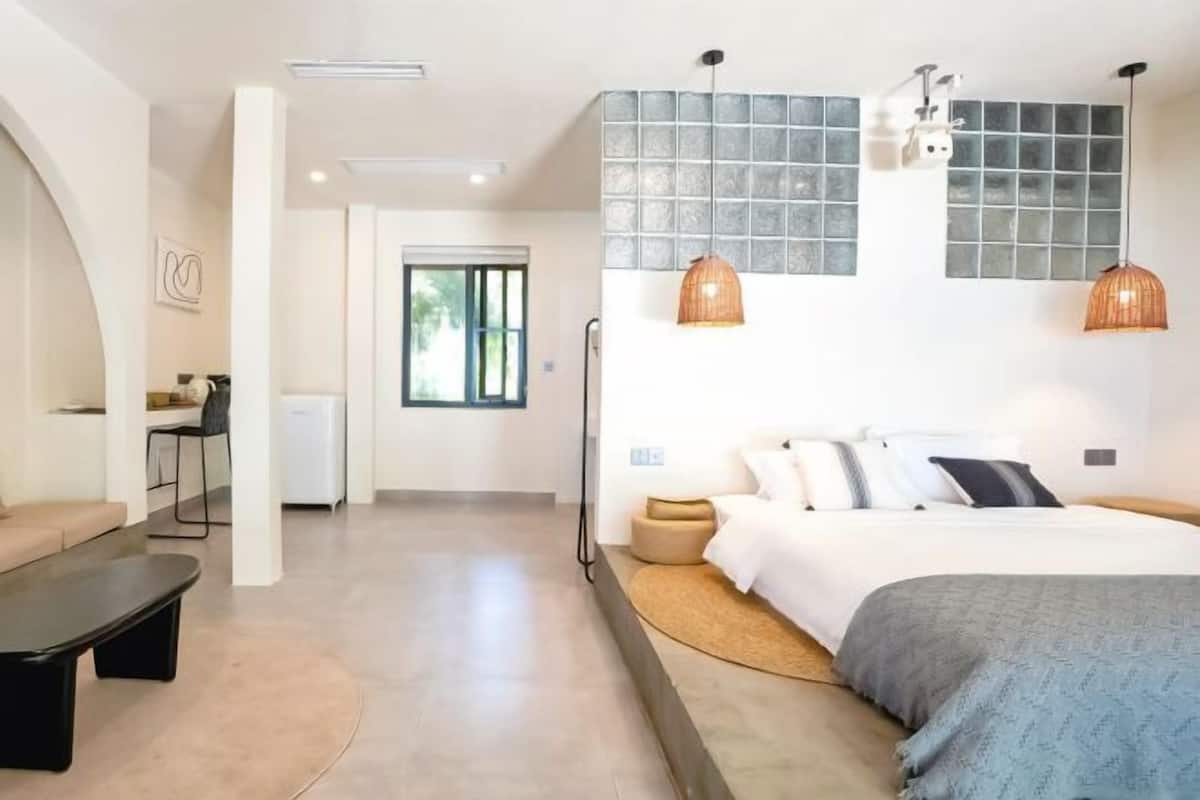 A modern bedroom with a bed, bedside tables, a sofa, and a dining area with chairs.