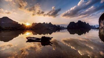 A boat on a calm lake with mountains in the background and the sun setting.