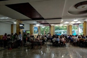 Un vaste espace de restauration intérieur, doté de hauts plafonds et de grandes fenêtres, comprenant de nombreuses tables et chaises disposées pour accueillir des groupes.