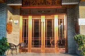 Une entrée de bâtiment traditionnel chinois, avec une porte en bois, deux chaises à l’extérieur et une enseigne au-dessus de la porte.