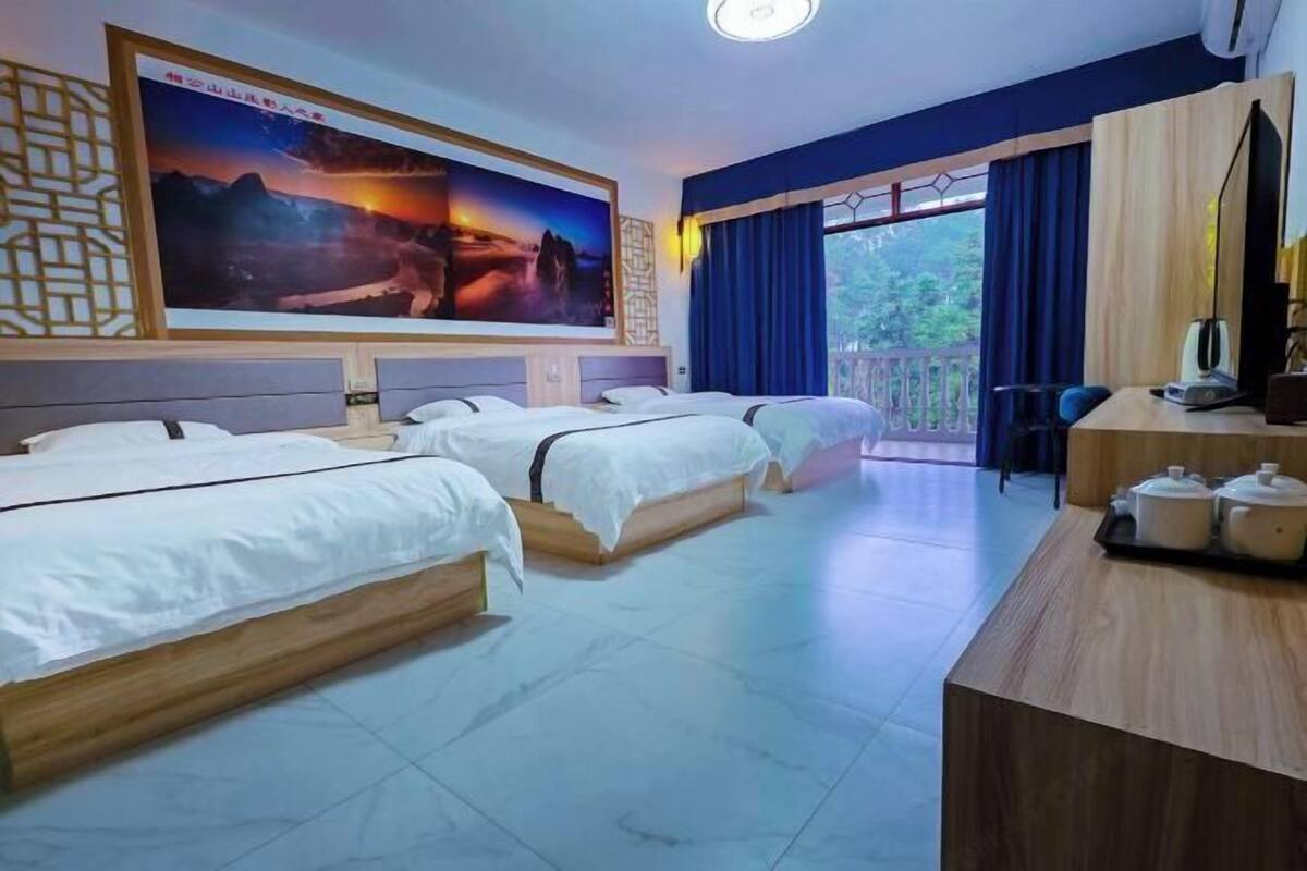 Una habitación de hotel con tres camas, un escritorio con computadora y un cuadro grande en la pared.