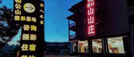 A hotel with a prominent red sign, a black signboard with yellow text, and a red carpet leading to the entrance.