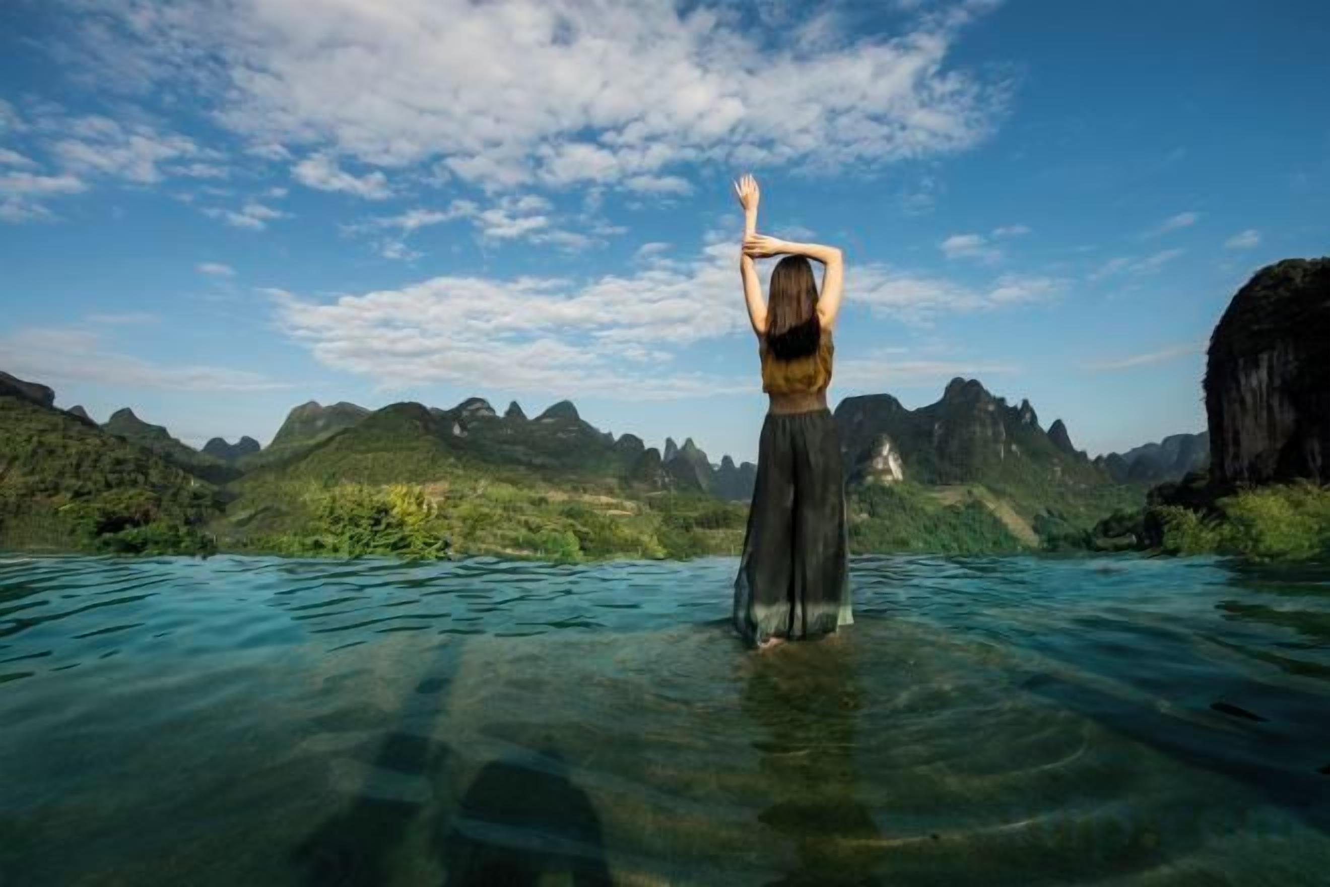 Una persona de pie en aguas transparentes, con un paisaje montañoso al fondo.