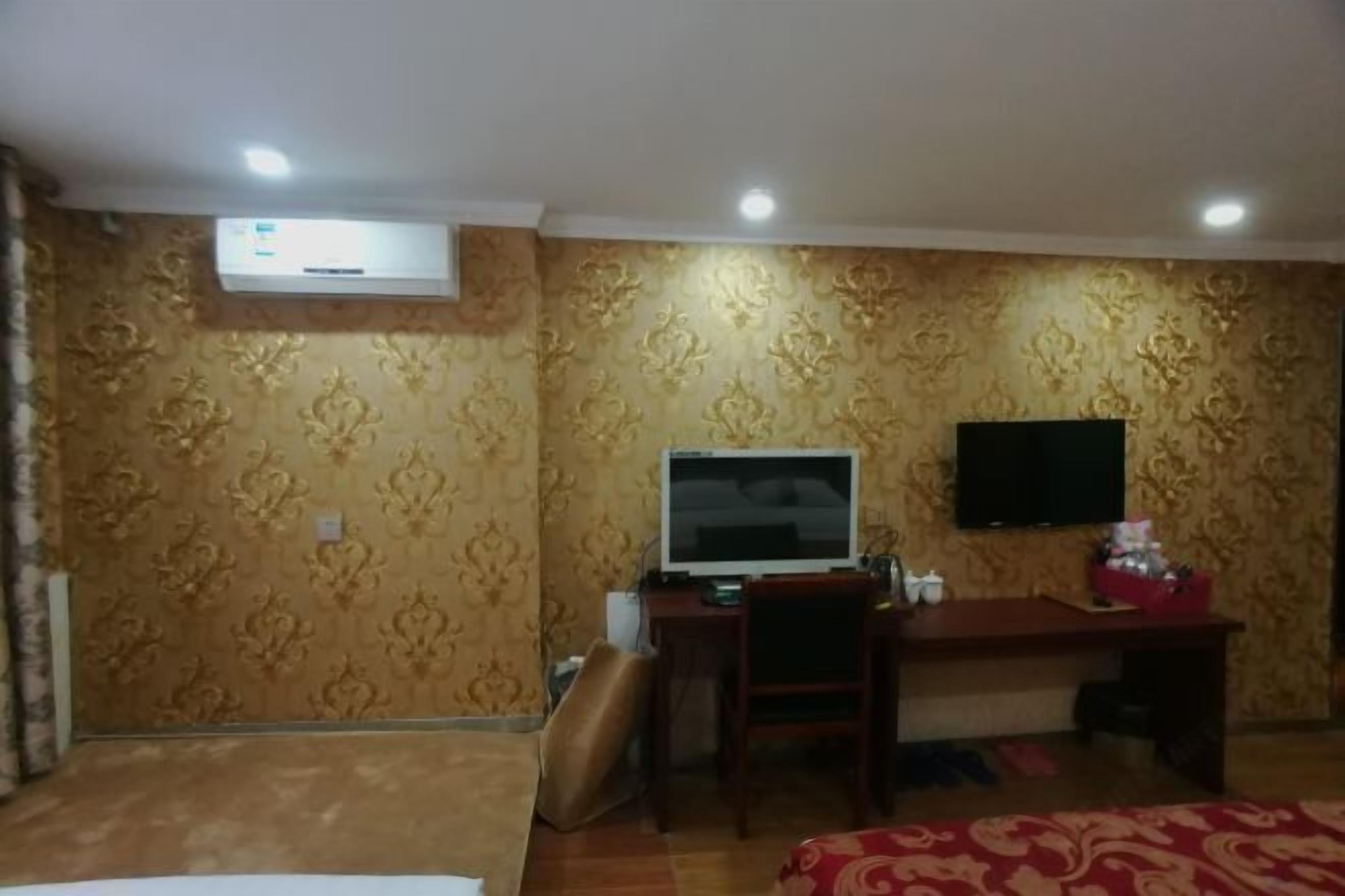 A hotel room with a bed, a desk, a television, and an air conditioning unit.