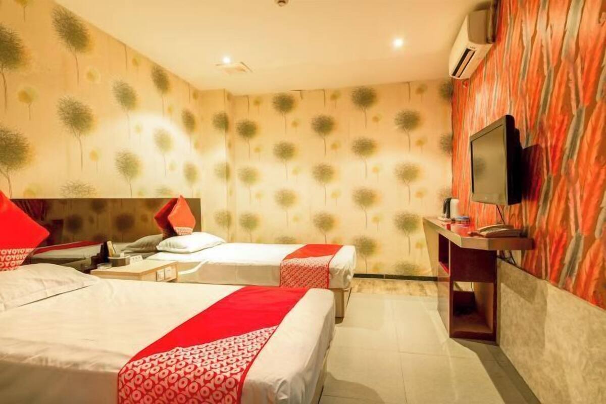 A hotel room with two beds, a desk, a TV, and a patterned wall.
