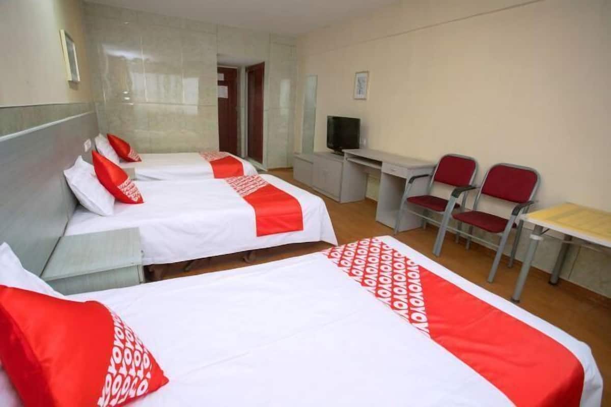 A hotel room with two beds, a desk, a television, and two red chairs.