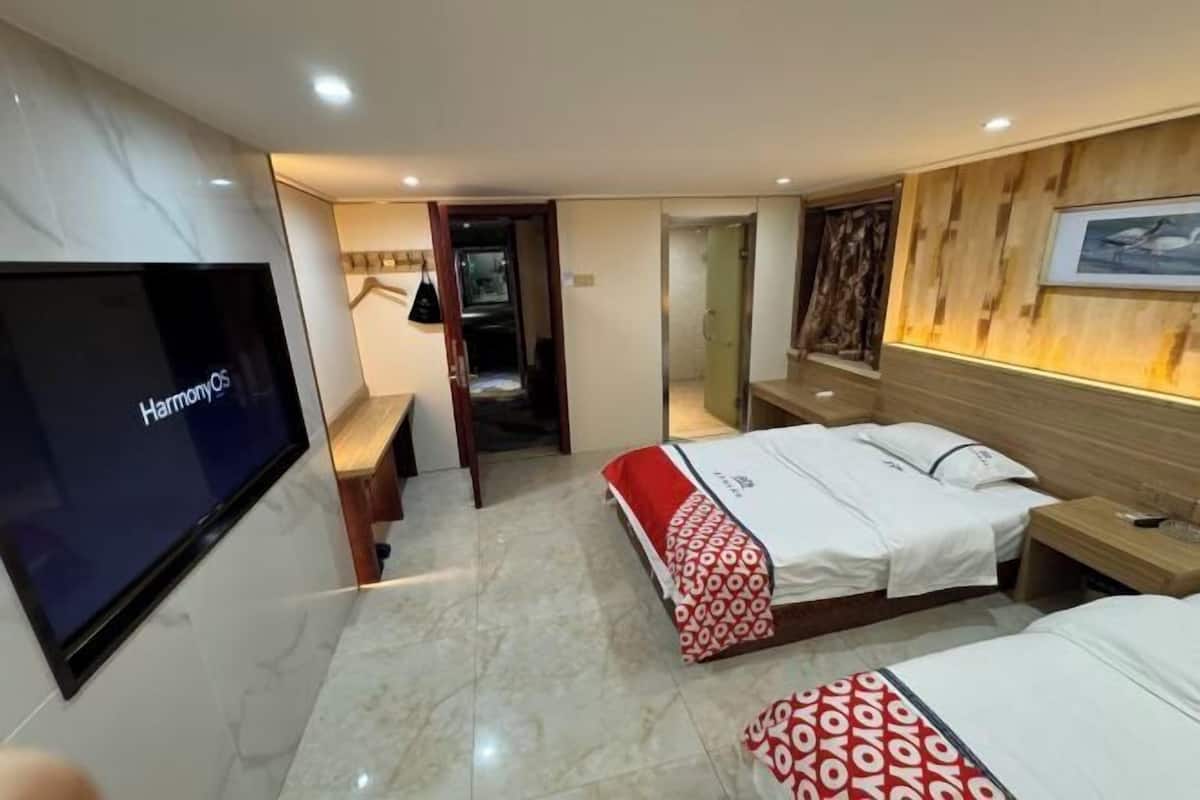 A hotel room with a TV, a bed with a red and white patterned bedspread, a wooden headboard, and a framed picture on the wall.