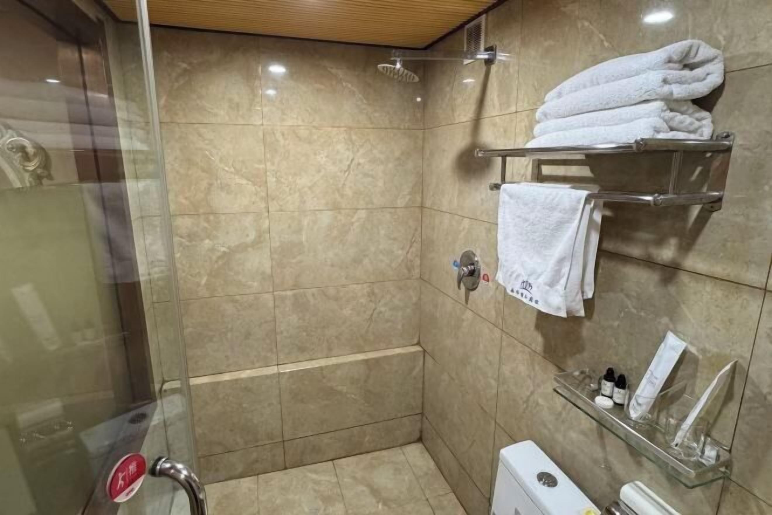 A shower area with a glass door, a towel rack with folded towels, and a shelf with toiletries.