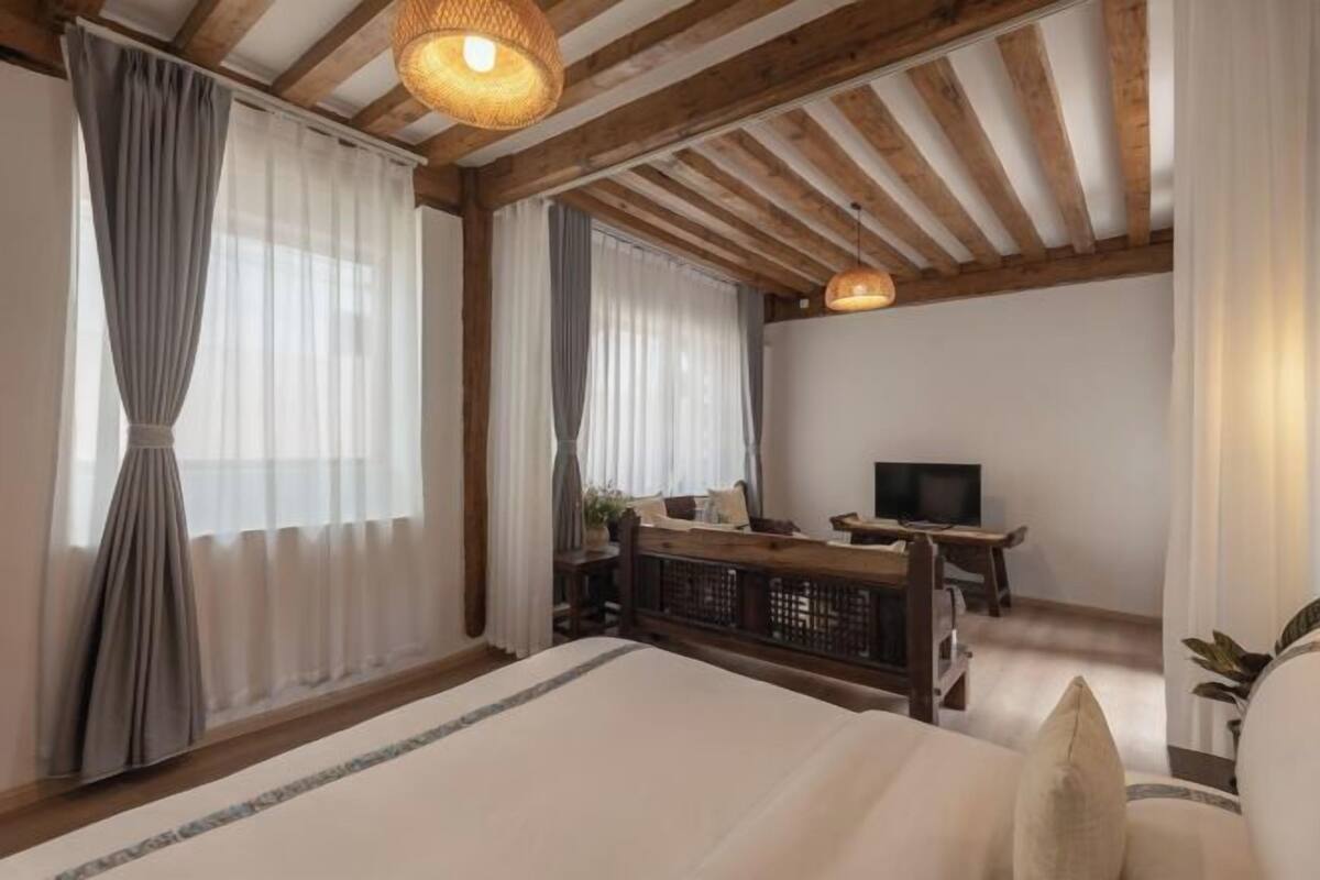A bedroom with a bed, a desk, a television, and a window with curtains.