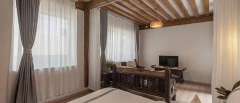Une chambre à coucher avec un lit, un bureau, une télévision et une fenêtre avec des rideaux.