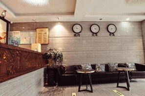 Ein modernes Interieur mit einer Rezeption, einer Couch, einem kleinen Tisch und drei Uhren an der Wand.