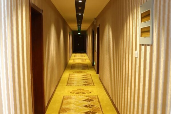 A hotel corridor with a carpeted floor, doors on both sides, and a light fixture on the ceiling. - Yichun Mantu Hotel (Yichun)