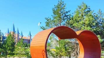 Una gran estructura de madera con diseño circular, frente a un fondo de árboles y un edificio parecido a un castillo.