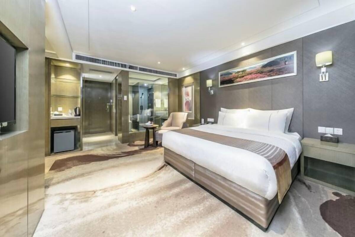 Habitación de hotel moderna con una cama grande, un escritorio pequeño, una silla, un espejo y un cuadro en la pared.