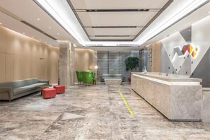 Un hall de hotel con mostrador de recepción, zona de estar y una planta.