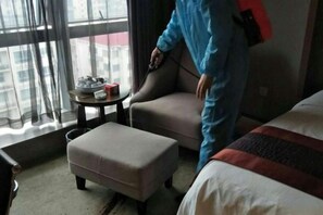 A hotel room with a sofa, a small table with a lamp, and a window with curtains.