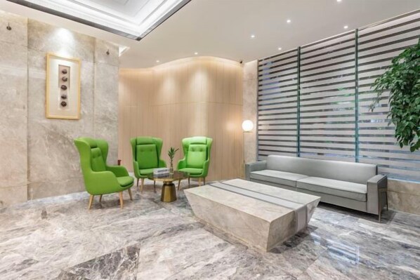 Un vestíbulo con piso de mármol, sillones verdes, un sofá gris y una planta.