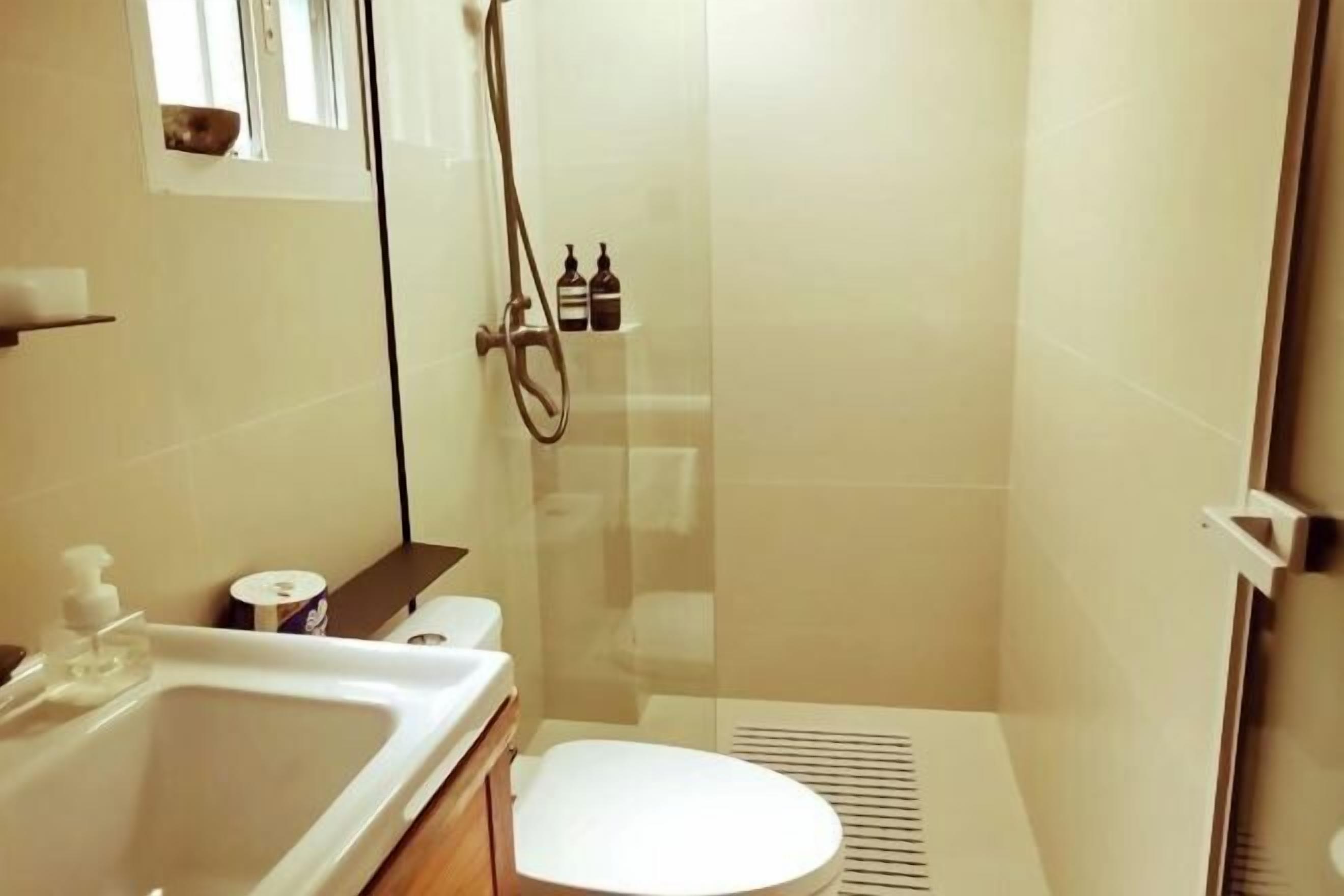 A bathroom with a toilet, sink, shower, and a small shelf with toiletries.