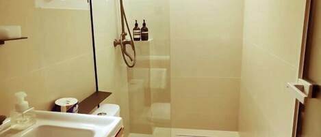 A bathroom with a toilet, sink, shower, and a small shelf with toiletries.