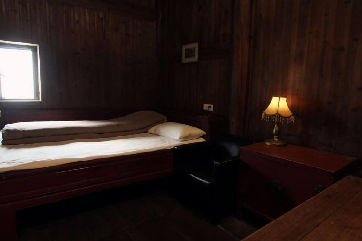 Ein Zimmer mit Holzboden, einem Bett, einem Sessel, einem Nachttisch und einer Lampe.