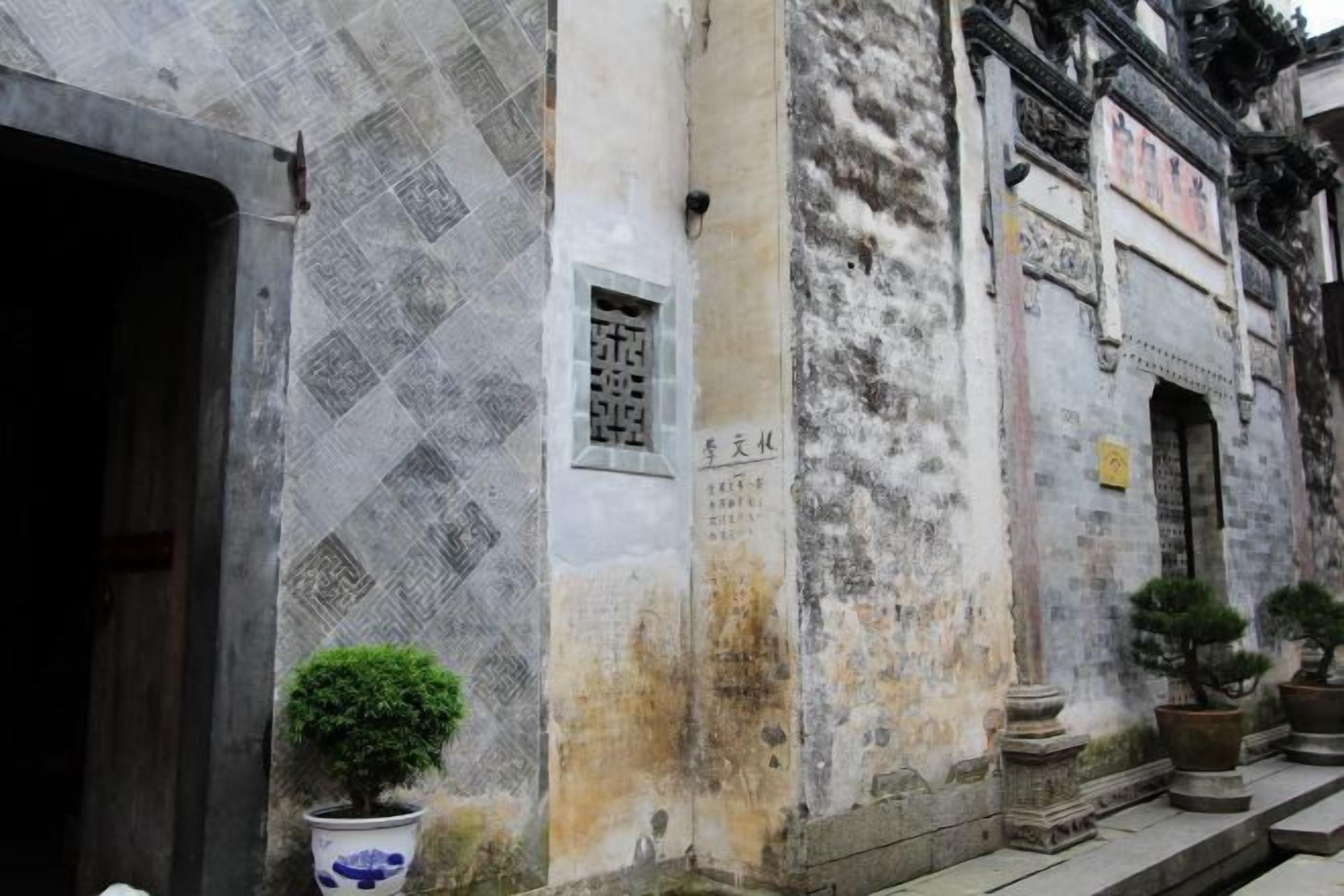 A traditional building with a tiled entrance, a small window with inscriptions, and potted plants.