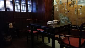 A traditional room with a wooden table and chairs, a window with a lattice design, and a wall with painted artwork.