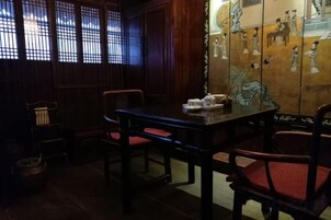 A traditional room with a wooden table and chairs, a window with a lattice design, and a wall with painted artwork.