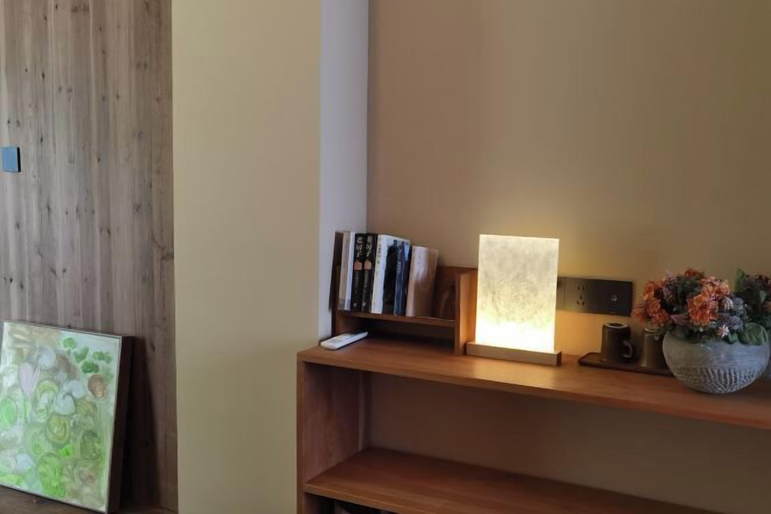 Una estantería de madera con libros, un cuadro enmarcado y un jarrón con flores.