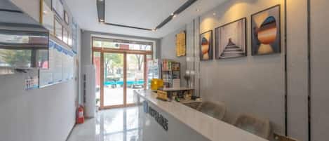 A modern hotel lobby with a reception desk, seating area, and a view of the outdoor pool.