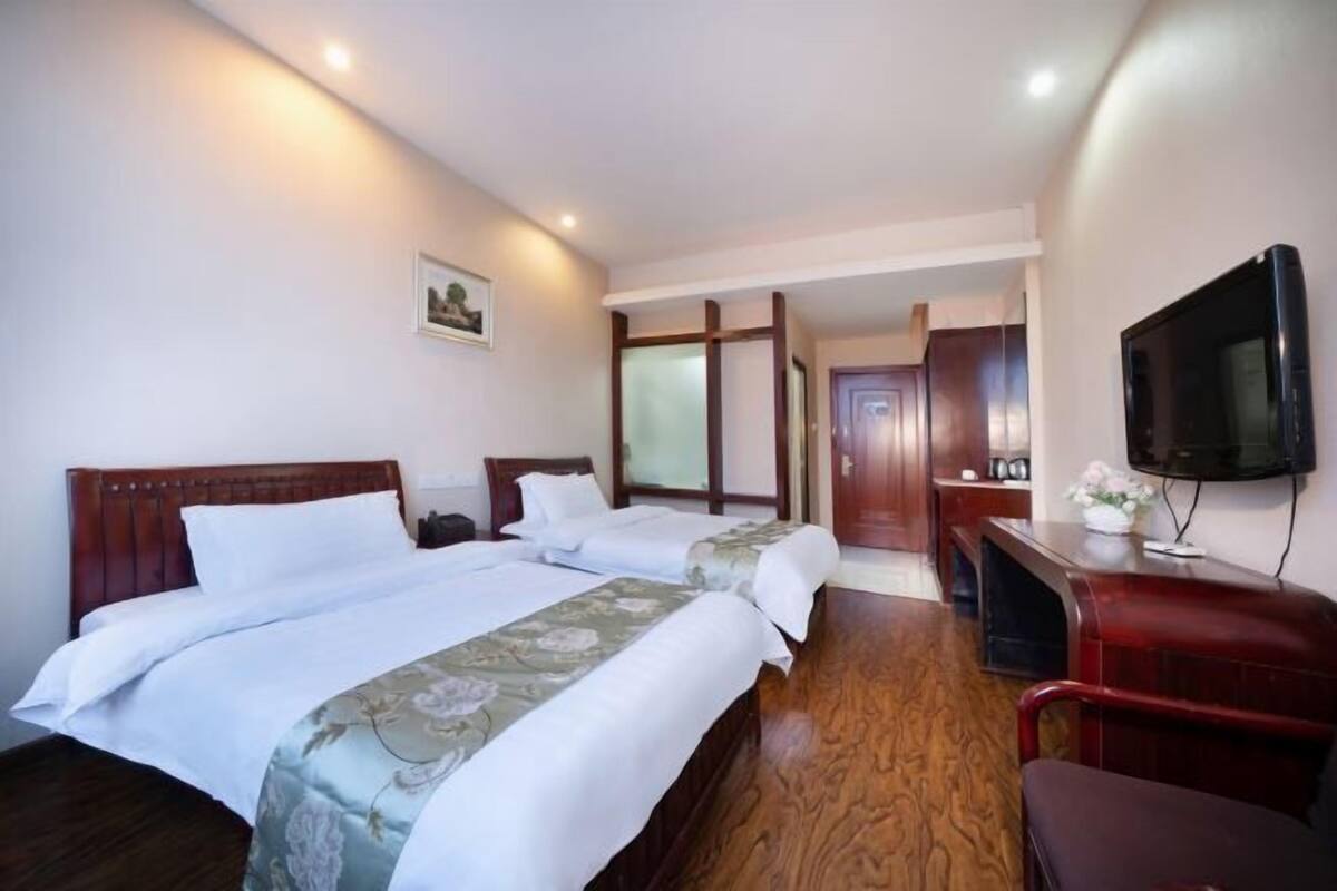 A hotel room with two beds, a TV, a desk, and a wooden floor.