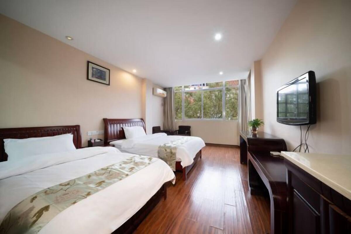 A hotel room with two beds, a TV, a desk, and a window with a view.