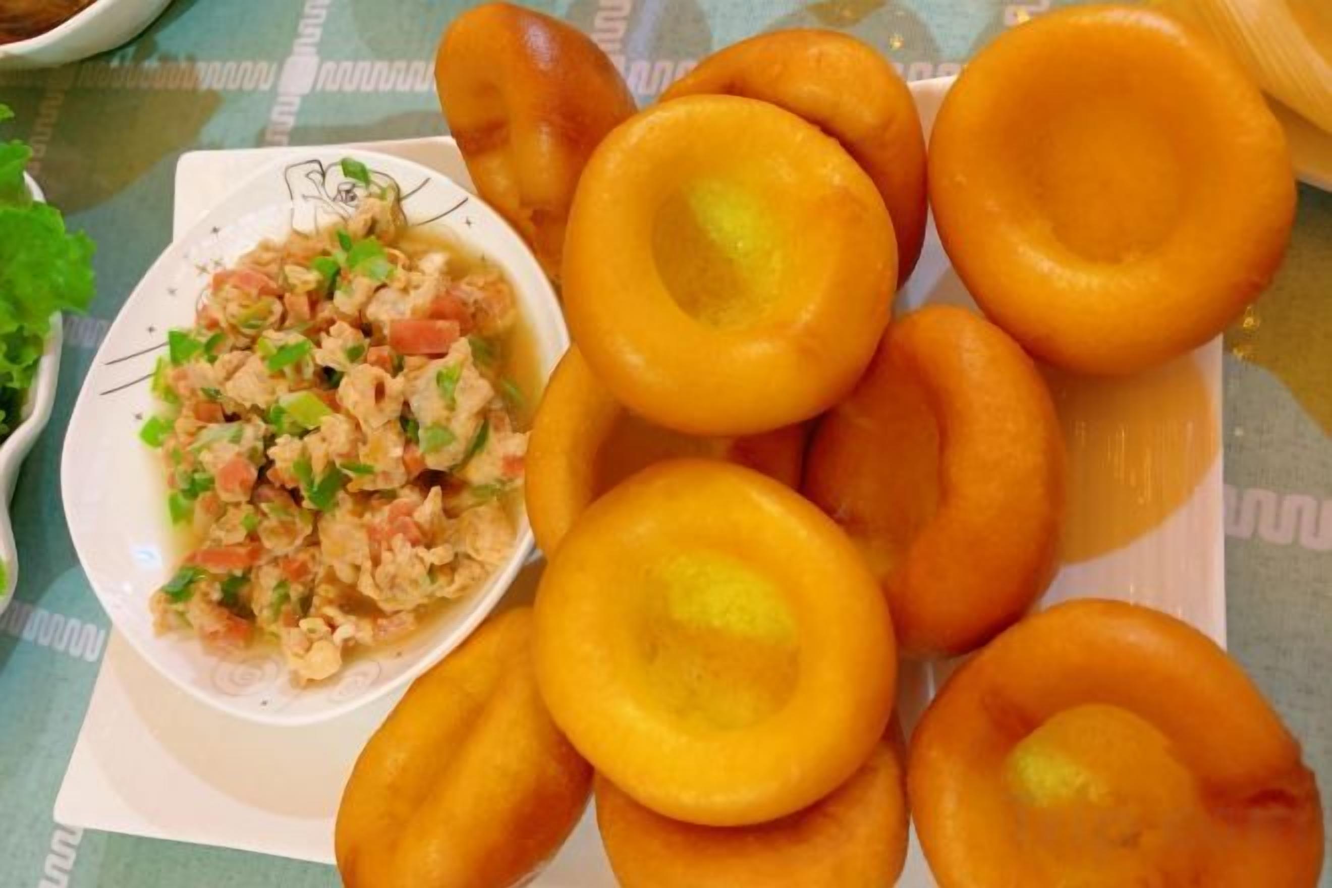 A plate of round, golden-brown fried items with a bowl of chopped vegetables and herbs.