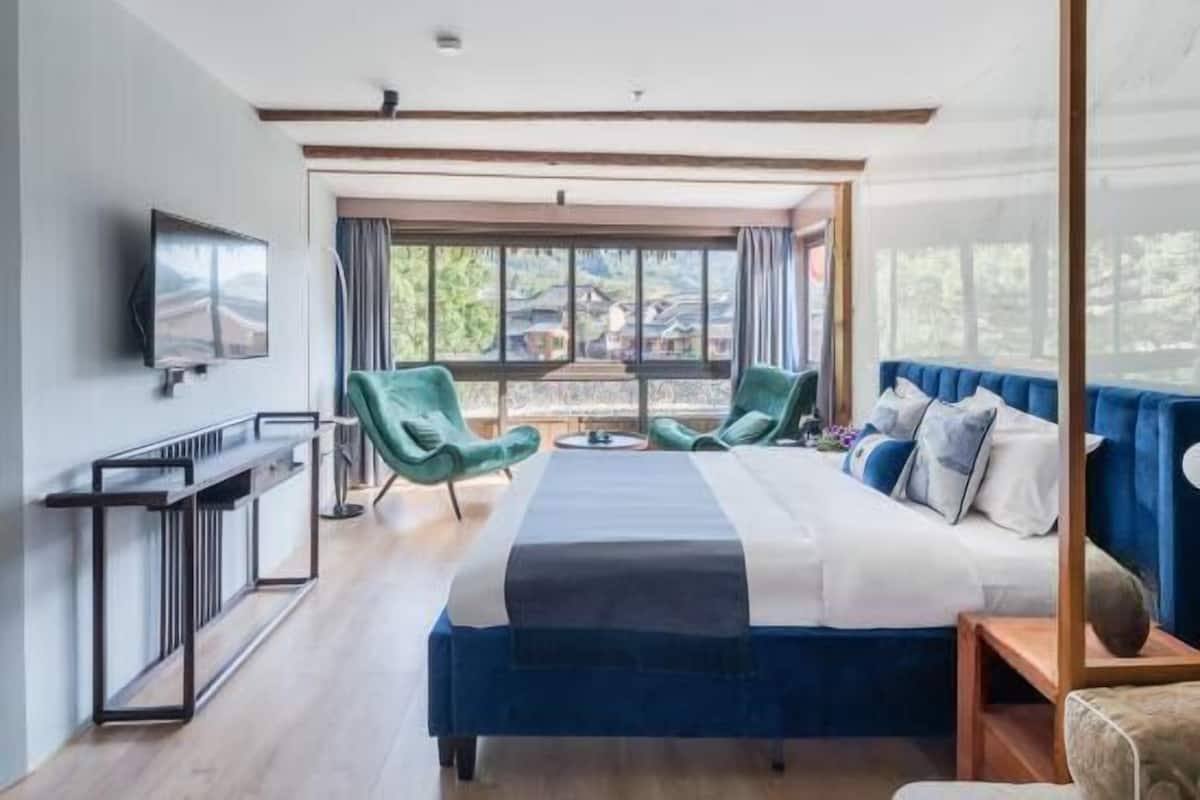 Een moderne hotelkamer met een groot bed, twee groene stoelen, een televisie en een balkon met uitzicht.