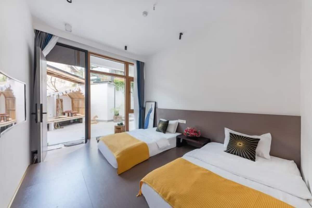 Een hotelkamer met twee bedden, een schuifglazen deur naar een buitenruimte, en een kleine tafel met een lamp.