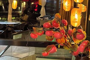 Interior de un restaurante con mesas, sillas, faroles decorativos y un separador de vidrio.