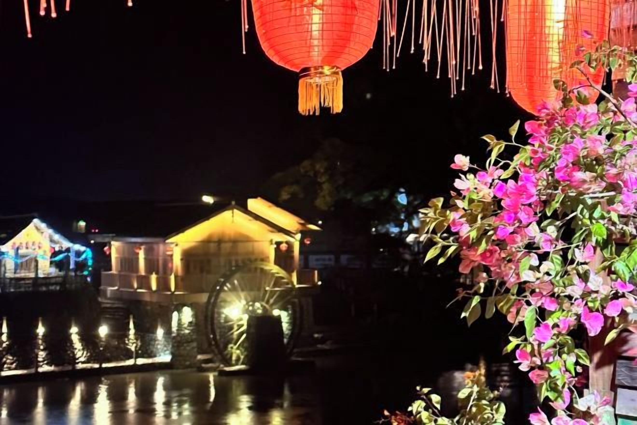 A traditional building with illuminated water wheels and red lanterns, suggesting a cultural or historical site.