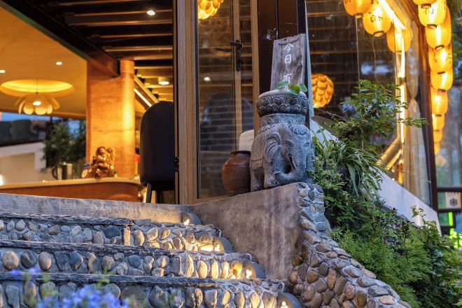 Una escalera de piedra que sube a la entrada de un edificio, con una figura decorativa de león de piedra y un jarrón grande en la parte superior.
