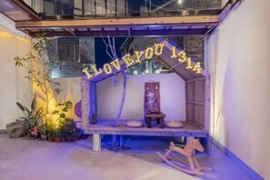 Un espace extérieur accueillant avec des sièges confortables, un panneau lumineux au néon, un cheval à bascule en bois et un petit banc.