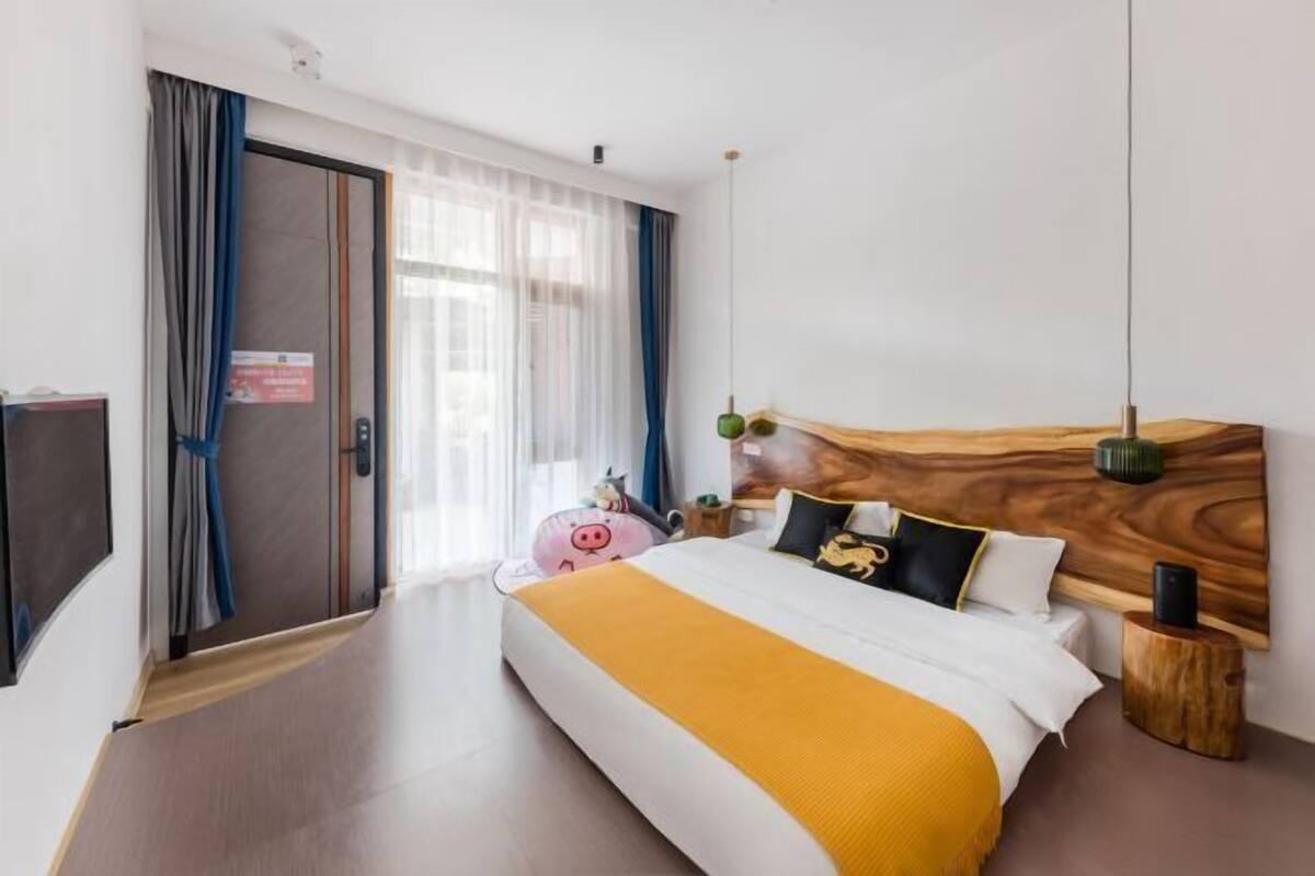 Een hotelkamer met een bed, een houten hoofdbord, een nachtkastje met een lamp, een televisie en een raam met gordijnen.