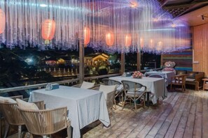 Un espace de restauration en plein air avec des tables et des chaises, une vue sur un bâtiment et des guirlandes lumineuses.