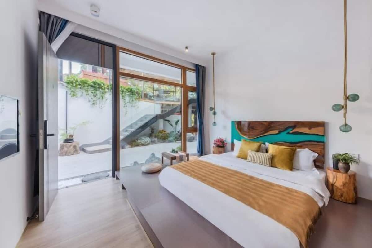 Een moderne slaapkamer met een groot bed, een schilderij en uitzicht op een trap en groen buiten.