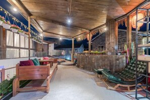 Un área de estar al aire libre con bancos de madera y una butaca acolchada, una valla de madera y un bar con mostrador y taburetes.