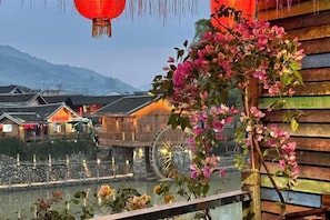 A traditional wooden building with a water wheel, a wooden fence, and a flowering plant. - Zaishui Yifang Motel (Nanjing County)