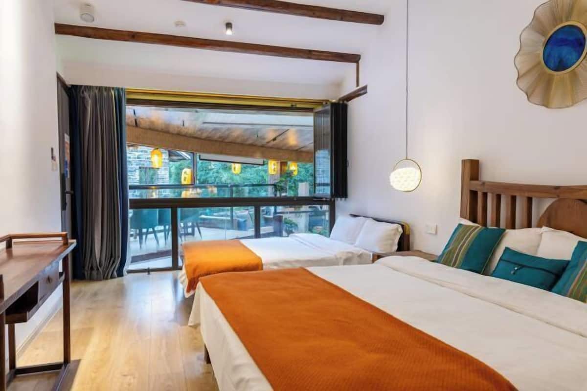 Een hotelkamer met twee bedden, een houten bureau, een groot raam met gordijnen en uitzicht op de omgeving.
