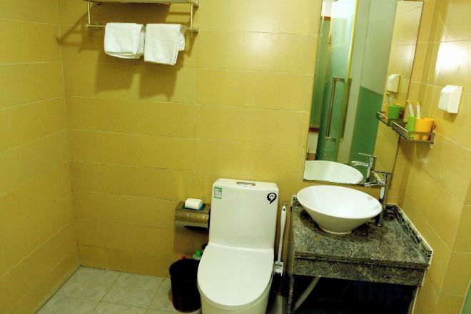Un baño con inodoro, lavamanos y espejo. Hay toallas en un perchero sobre el inodoro.